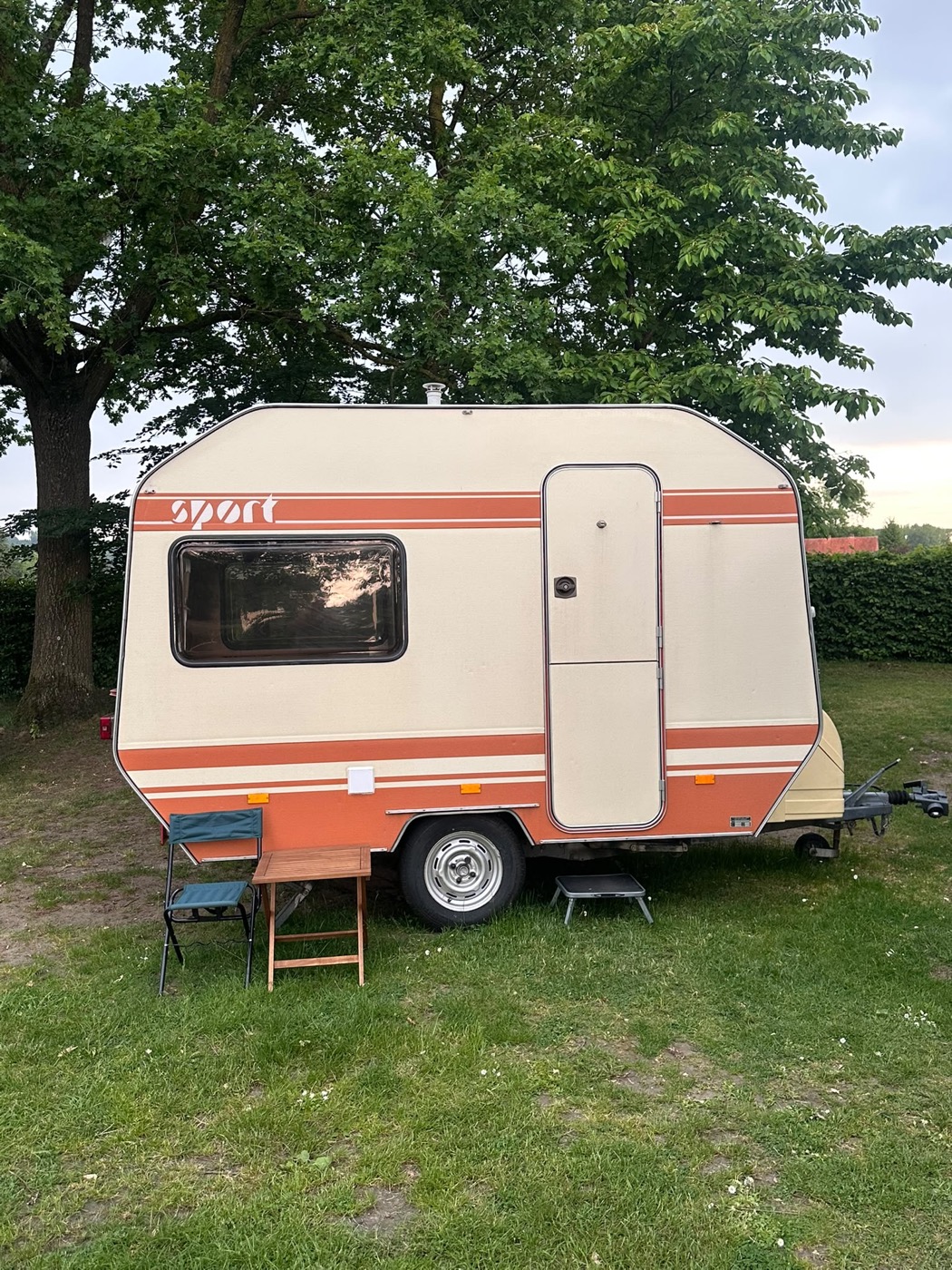 Wilky – Vintage-Wohnwagen Außenansicht mit Sitzgelegenheit unter Bäumen